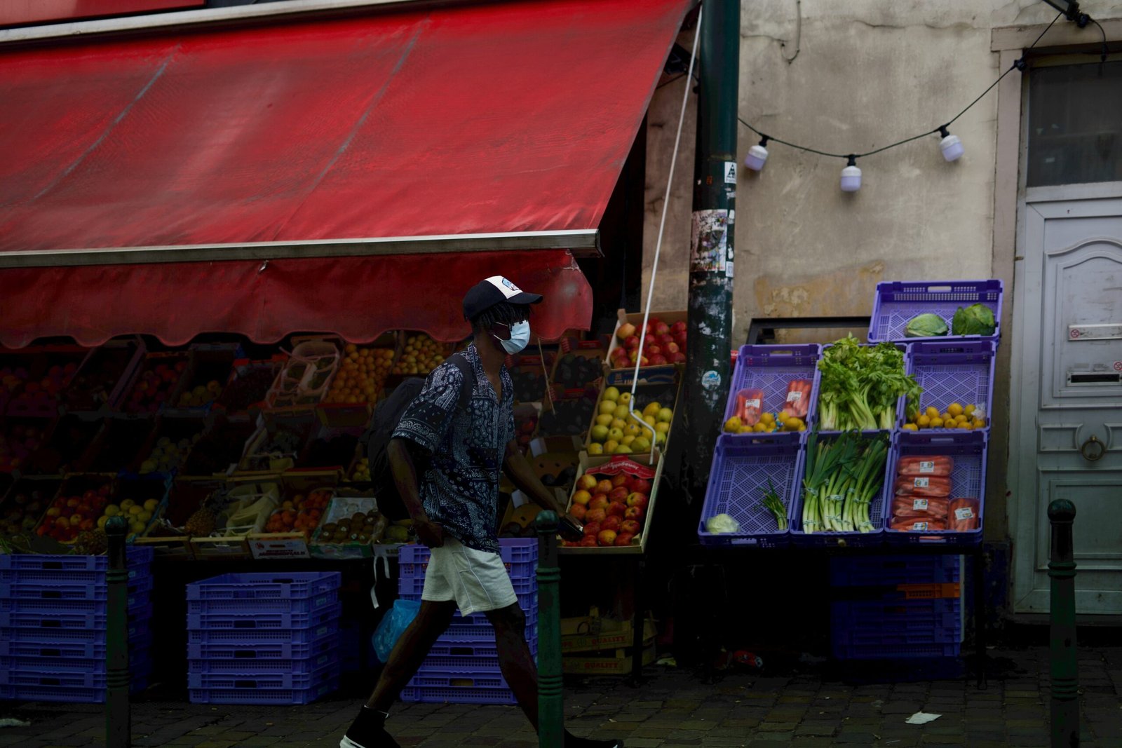 man in black and gray long sleeve shirt and blue denim jeans standing near fruit stand